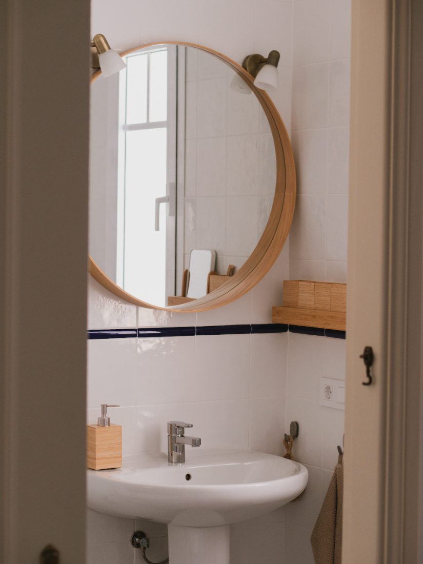 Bathroom with a round wooden mirror, white tiles and a navy tile border