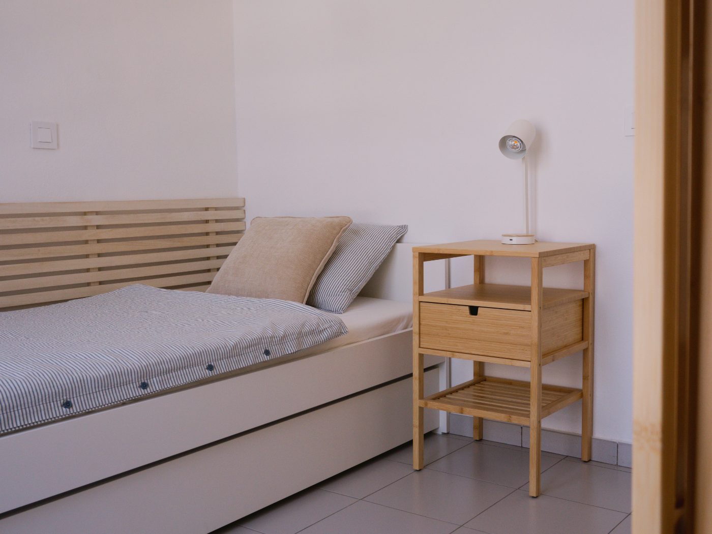 Single bed with striped linen, a slatted wood headboard and a bamboo bedside table