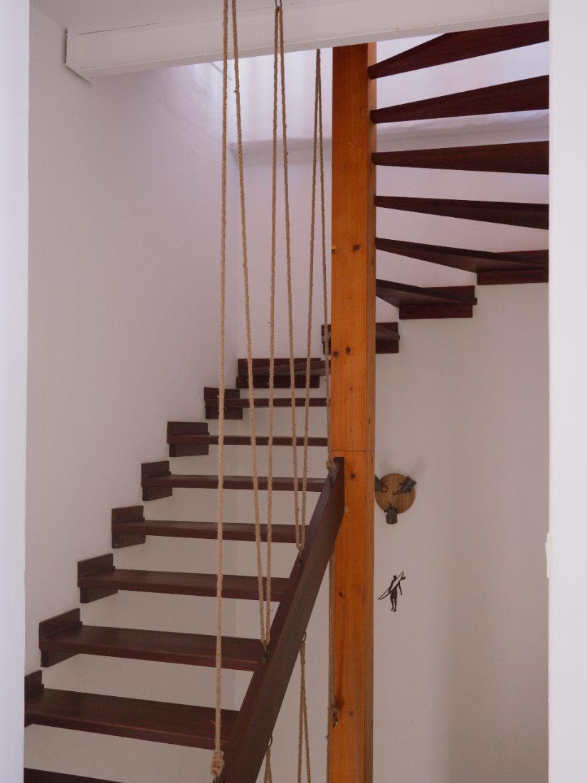 Open wooden staircase with a rope balustrade winding up through the house