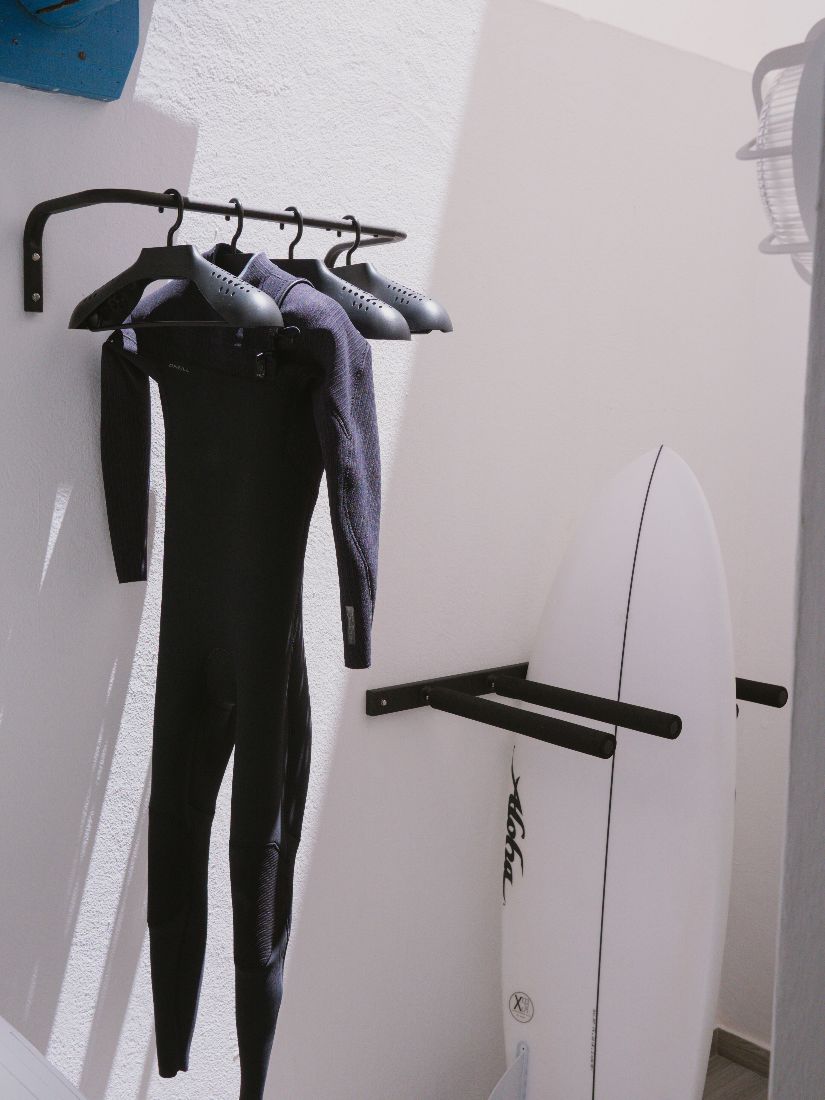Wetsuits and a surfboard on the rack by the outdoor shower