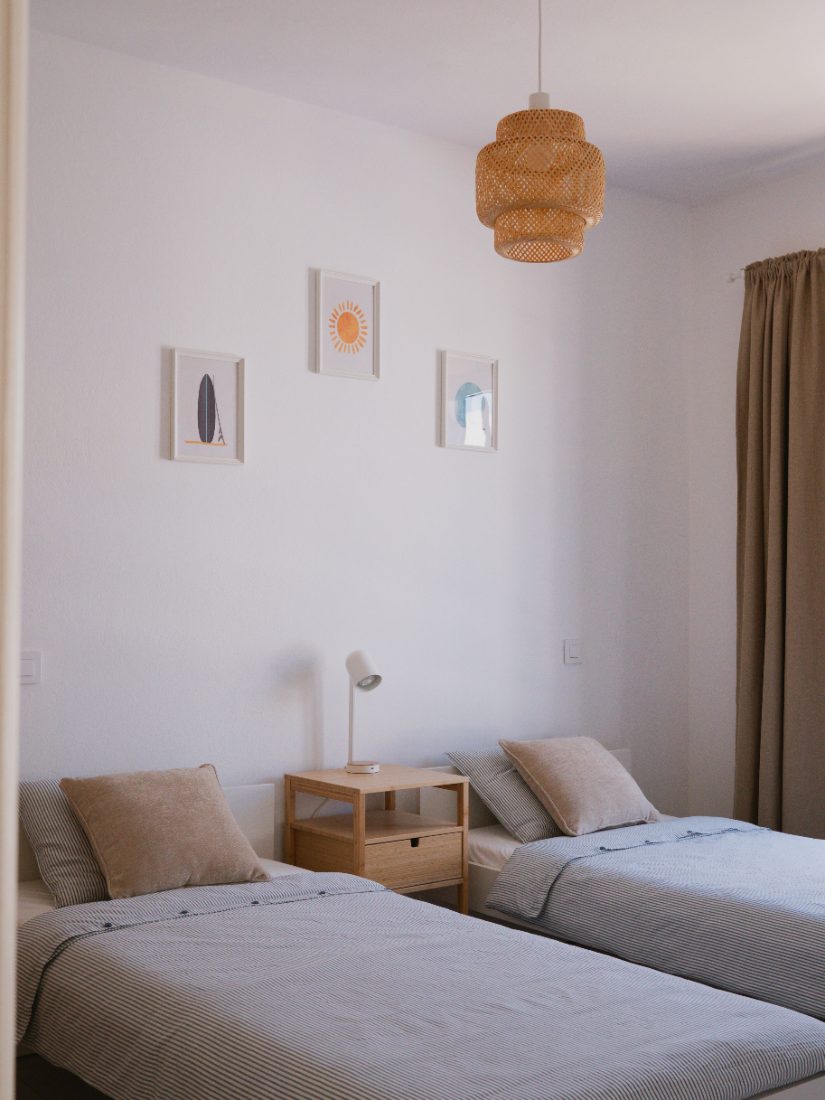 Twin beds with striped linen under a woven pendant lamp